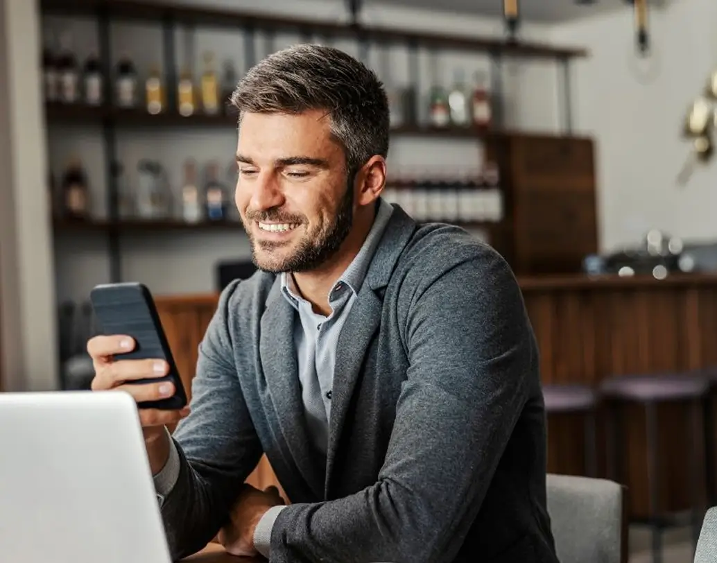Homem usando celular em café com notebook ilustrando como é fácil fazer um Pix com sua conta Cresol